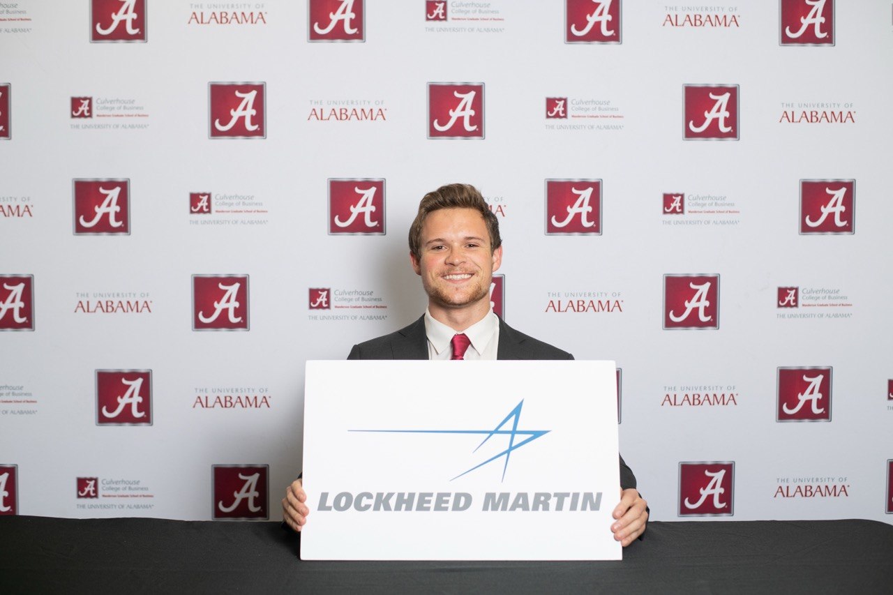 Jack Pierson at MBA graduation, holding a Lockheed Martin sign